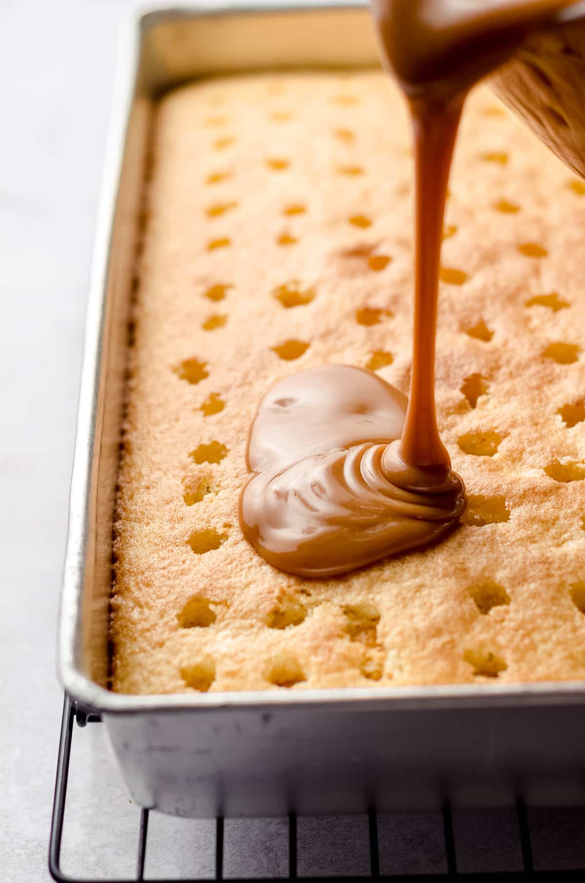 Pouring caramel sauce on top of a poke cake.