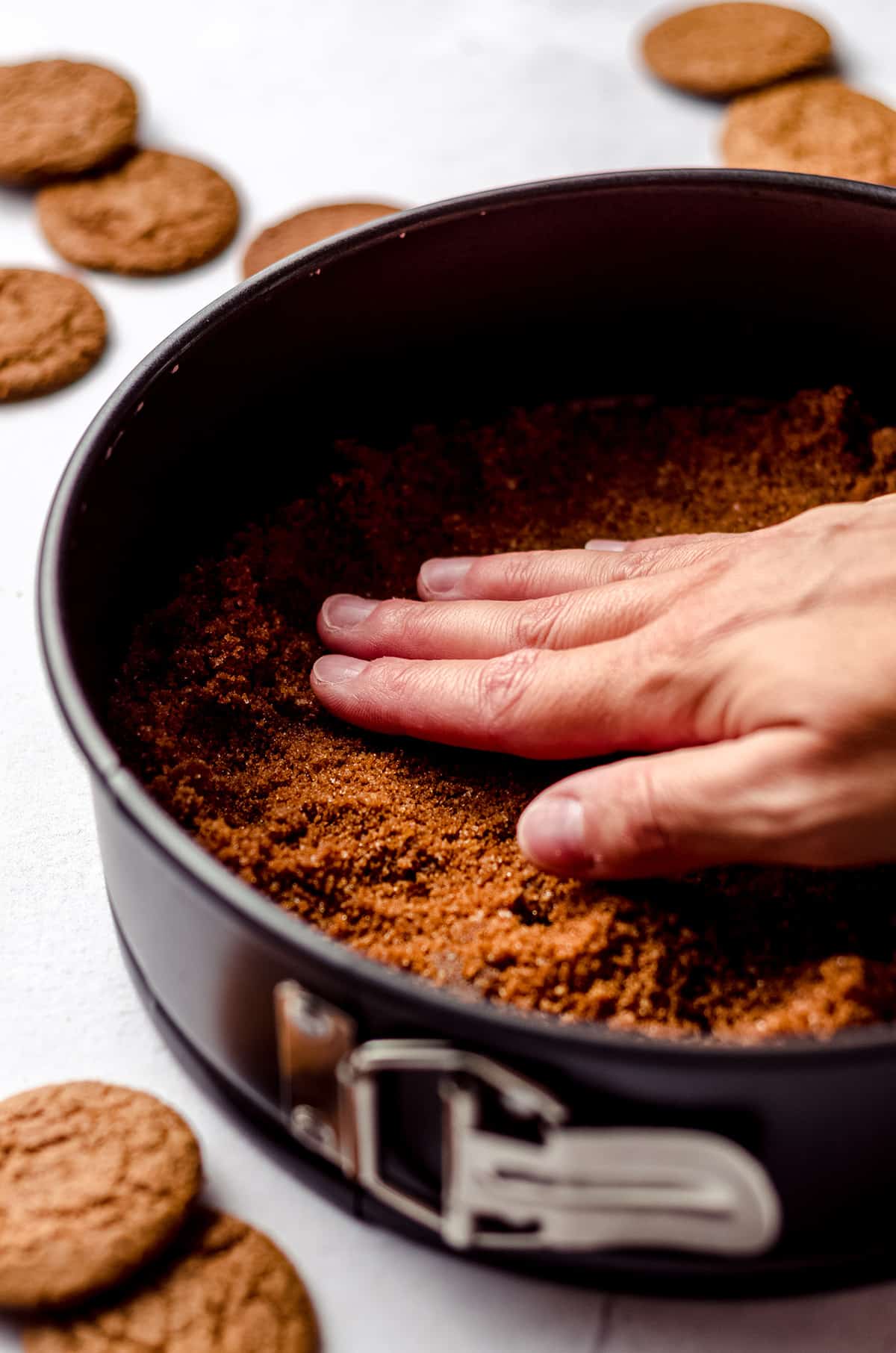 Patting a gingersnap crust into a springform pan.