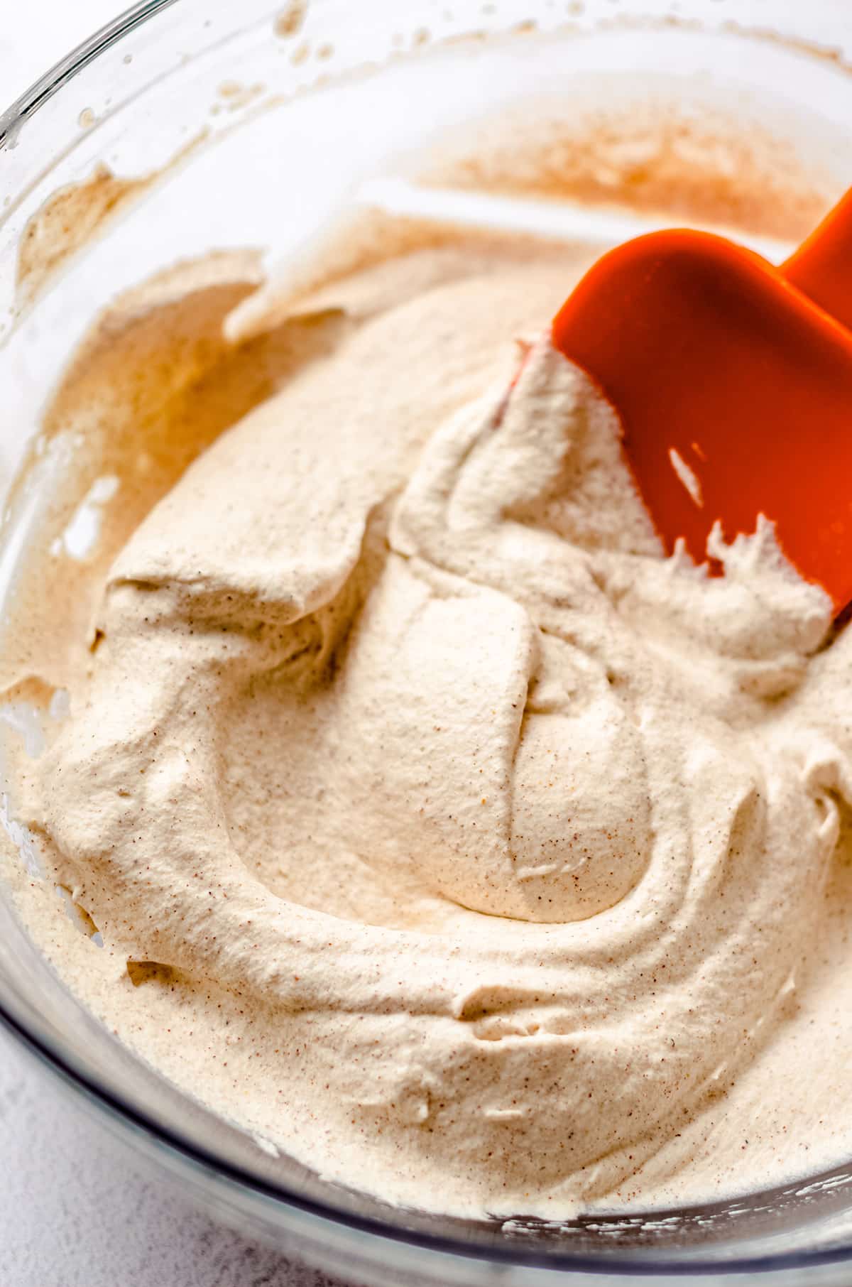 pumpkin spice whipped cream in a bowl spread around with an orange spatula
