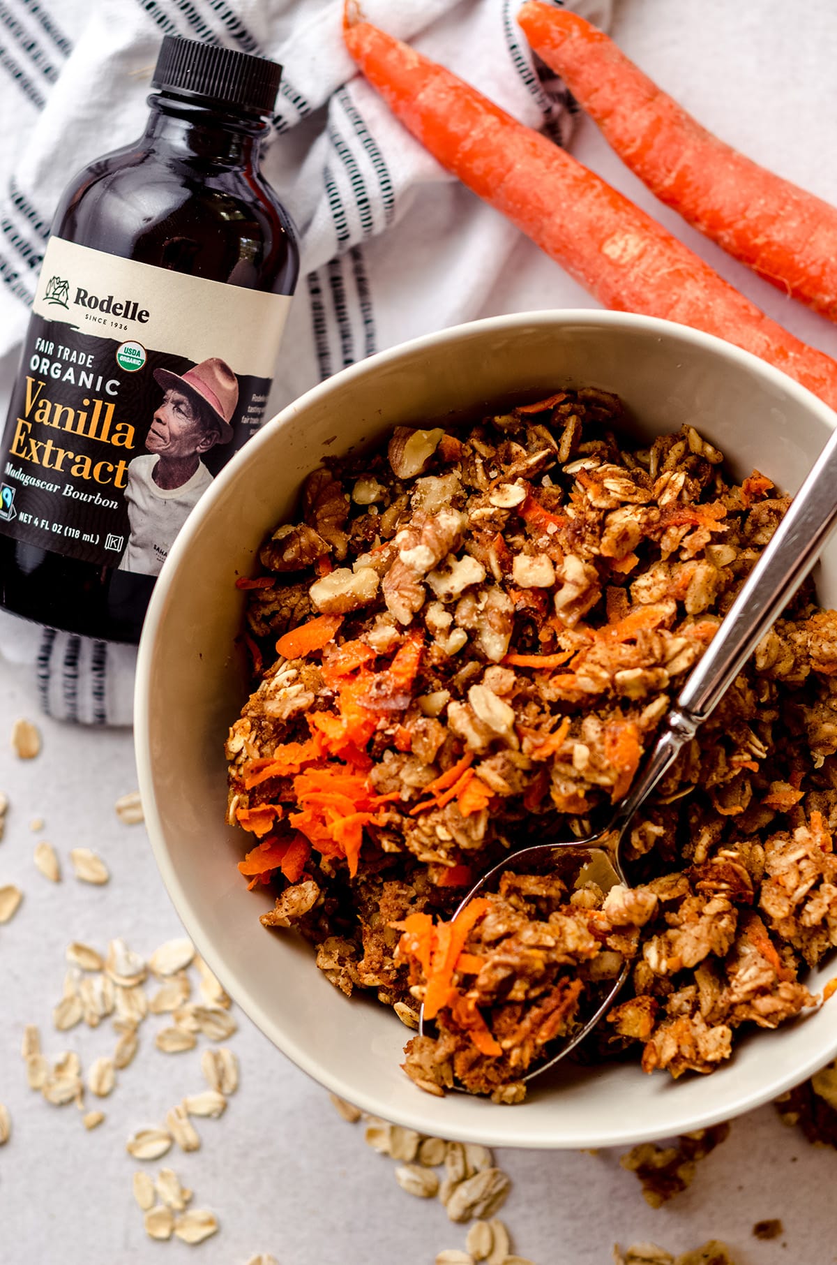 carrot cake baked oatmeal in a bowl with a spoon and a bottle of rodelle fair trade vanilla extract in the background