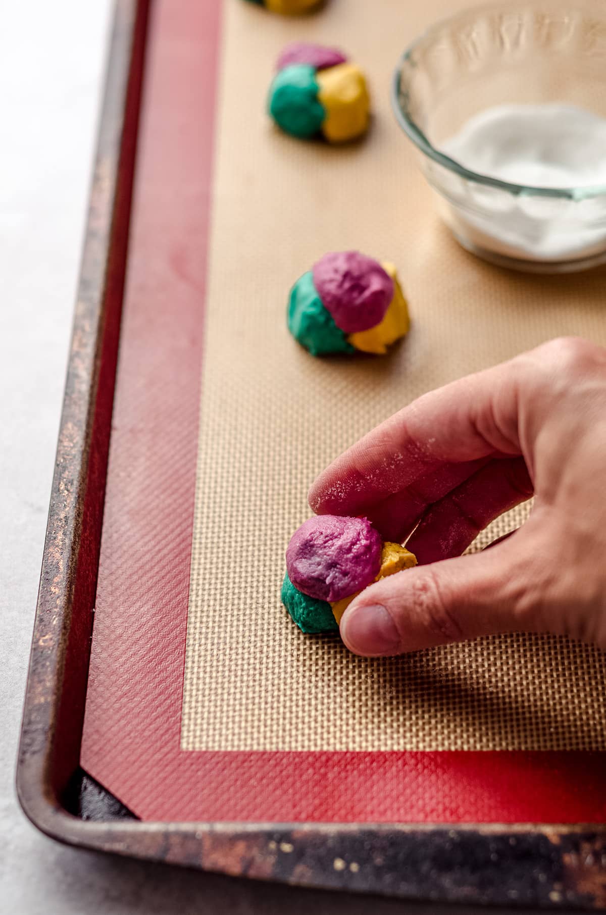 a hand shaping balls of colorful cookie dough on a baking sheet to make sally stitches cookies