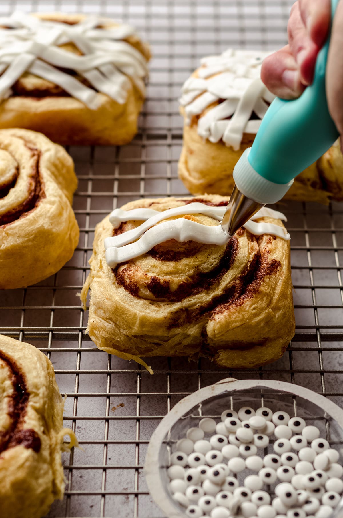 piping mummy wrap onto a cinnamon roll to make a cinnamon roll mummy