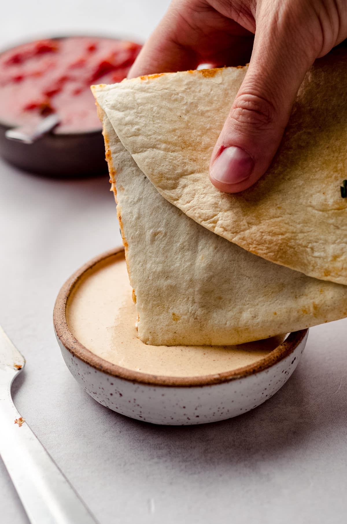 dipping sheet pan quesadillas into quesadilla sauce