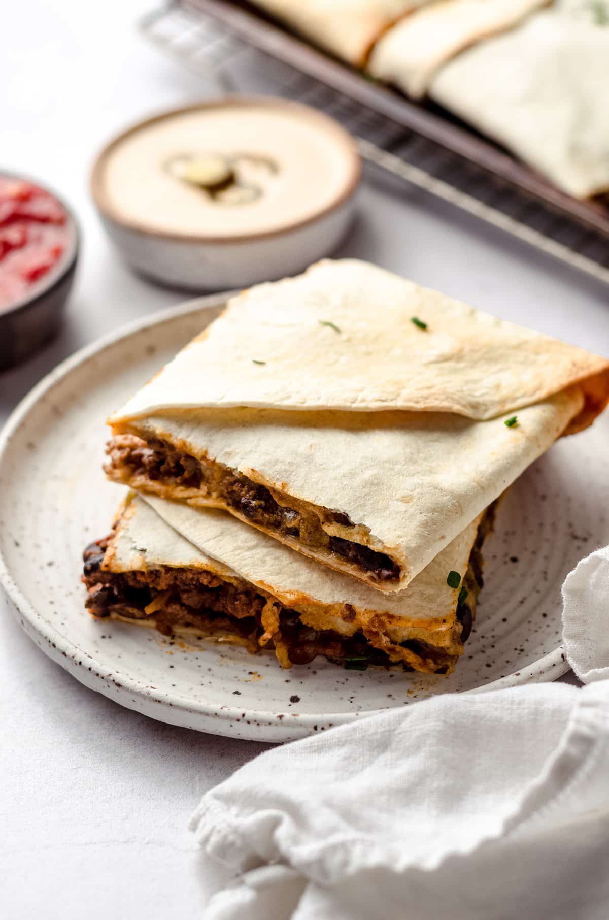 Two squares of quesadilla with bowls of sauce in the background.