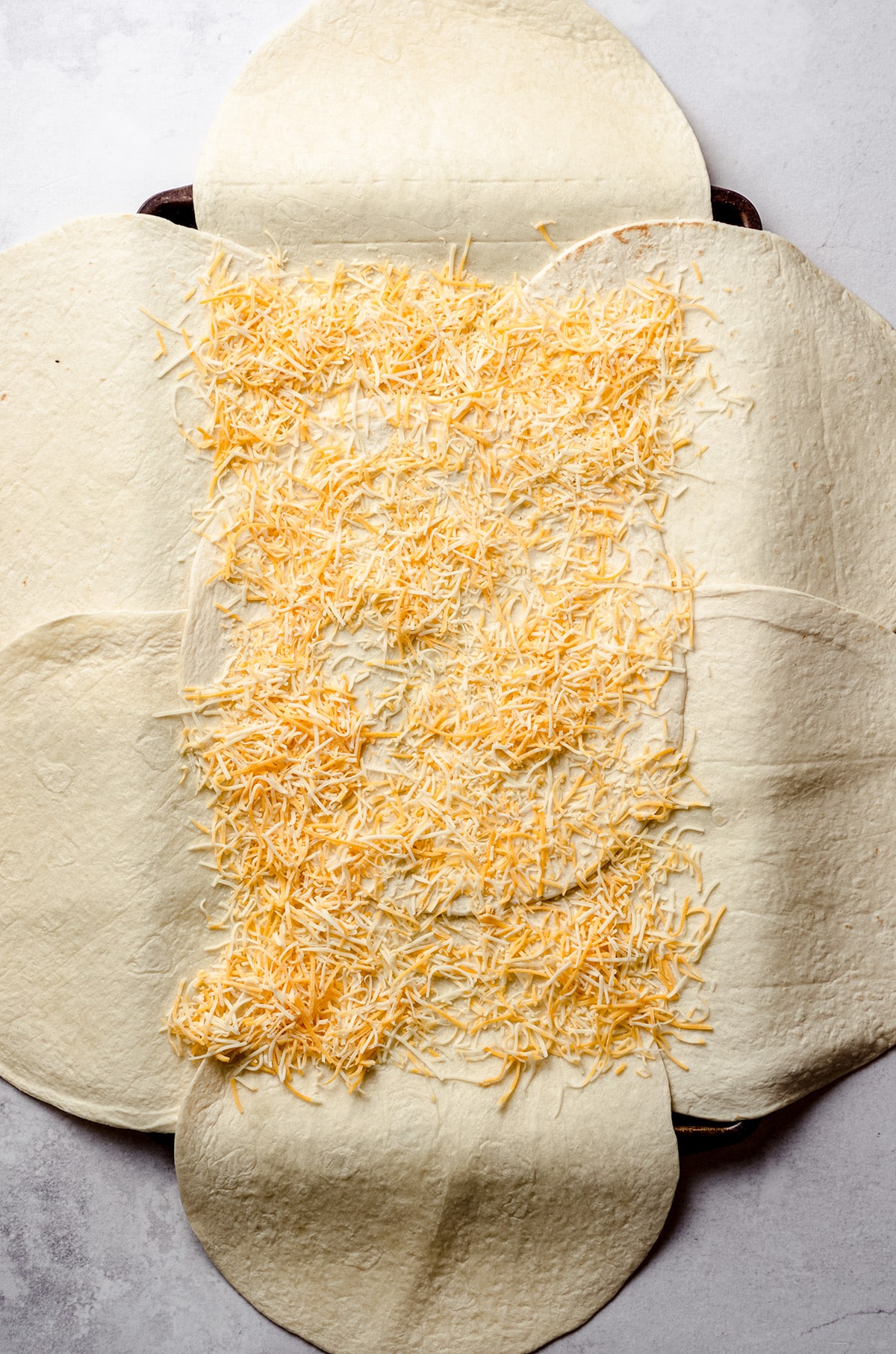 Adding shredded cheese to a sheet pan layered with tortillas.