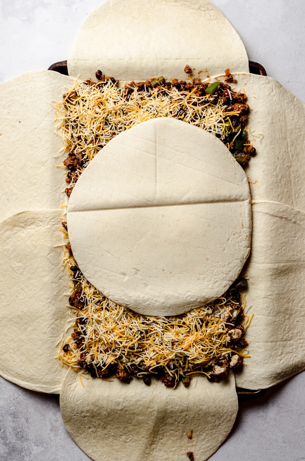 Adding a tortilla on top of a giant sheet pan quesadilla.