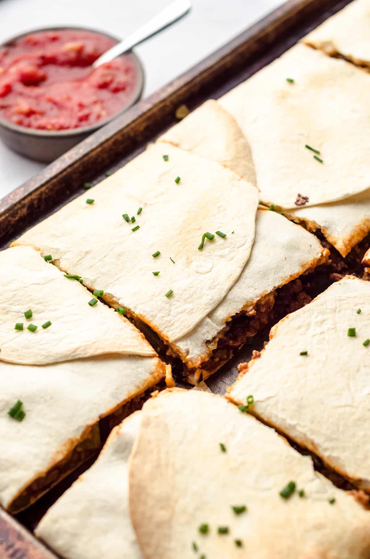 A sheet pan filled with square flour tortilla wrapped quesadillas.