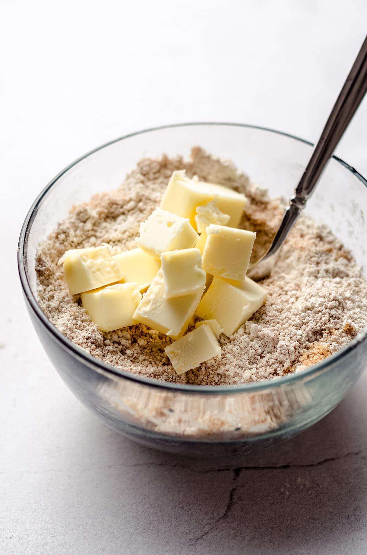 Adding cold butter to a bowl with a crumb mixture.