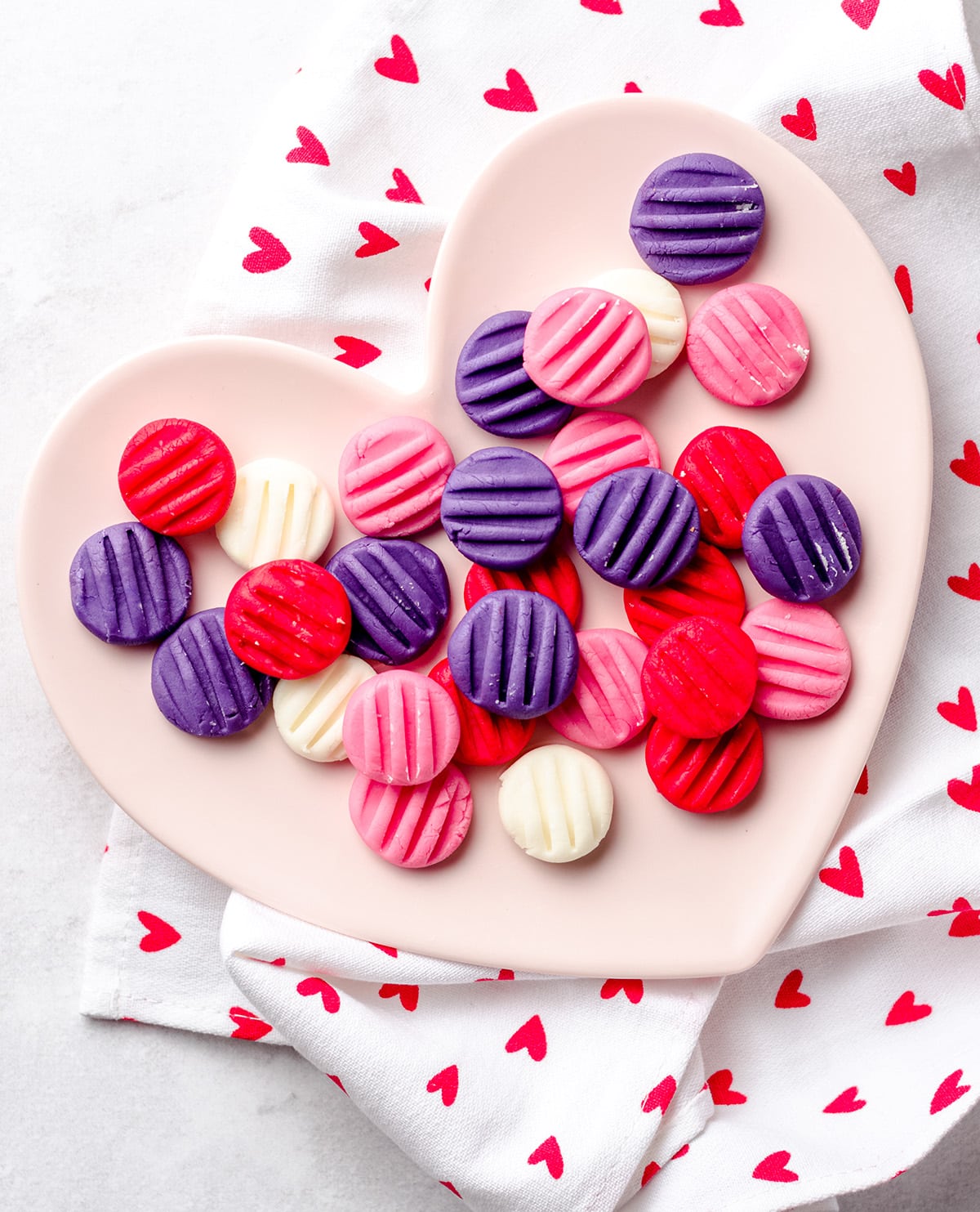 A heart shaped plate with pint, purple, red and white cream cheese mints.