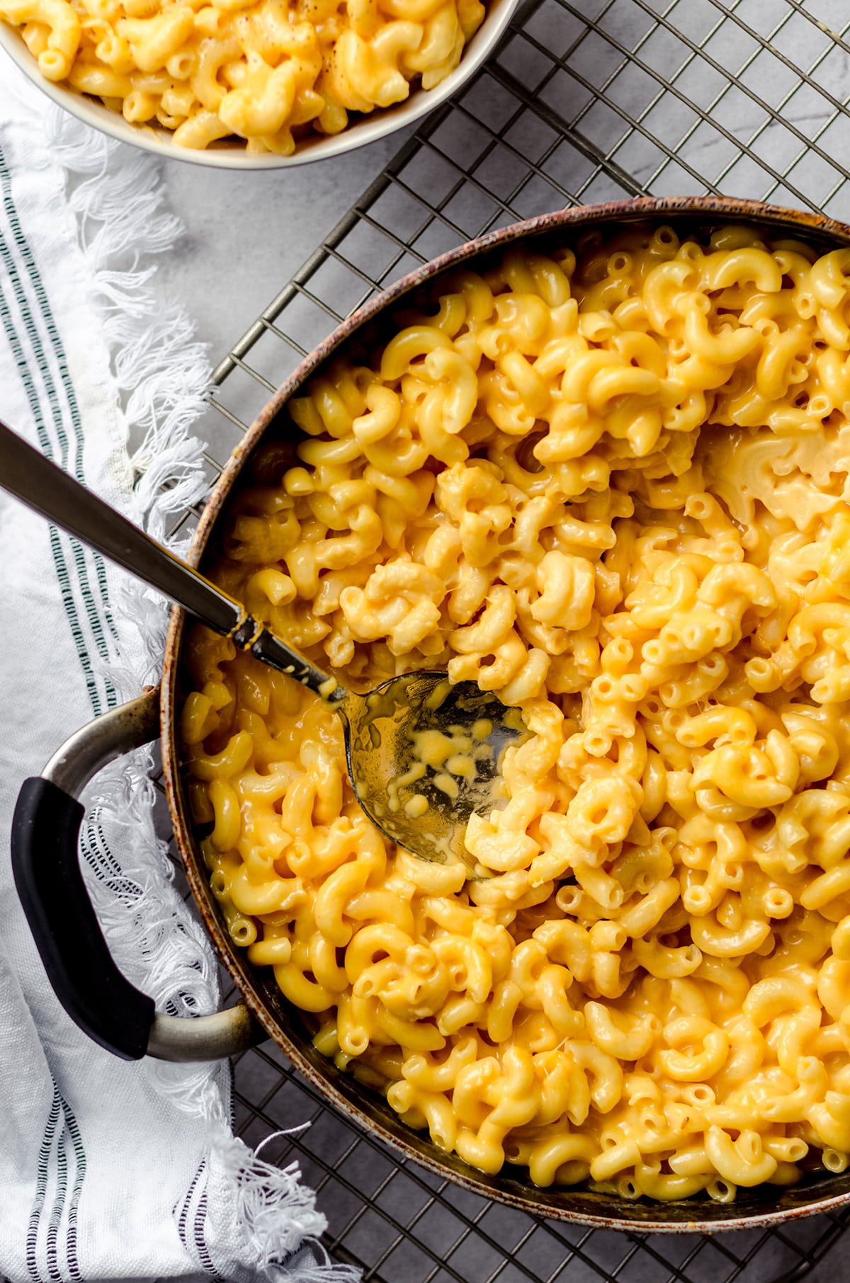 A pot with macaroni and cheese, with a serving bowl in the corner.