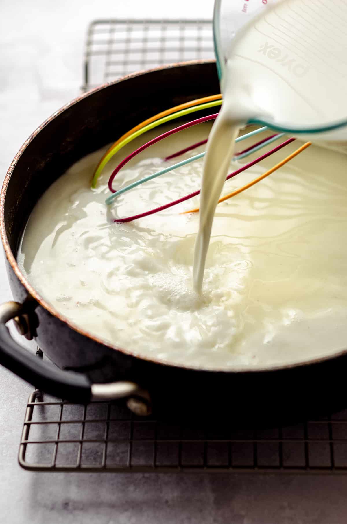 Adding milk to a saucepan with a roux, to form a thick sauce.