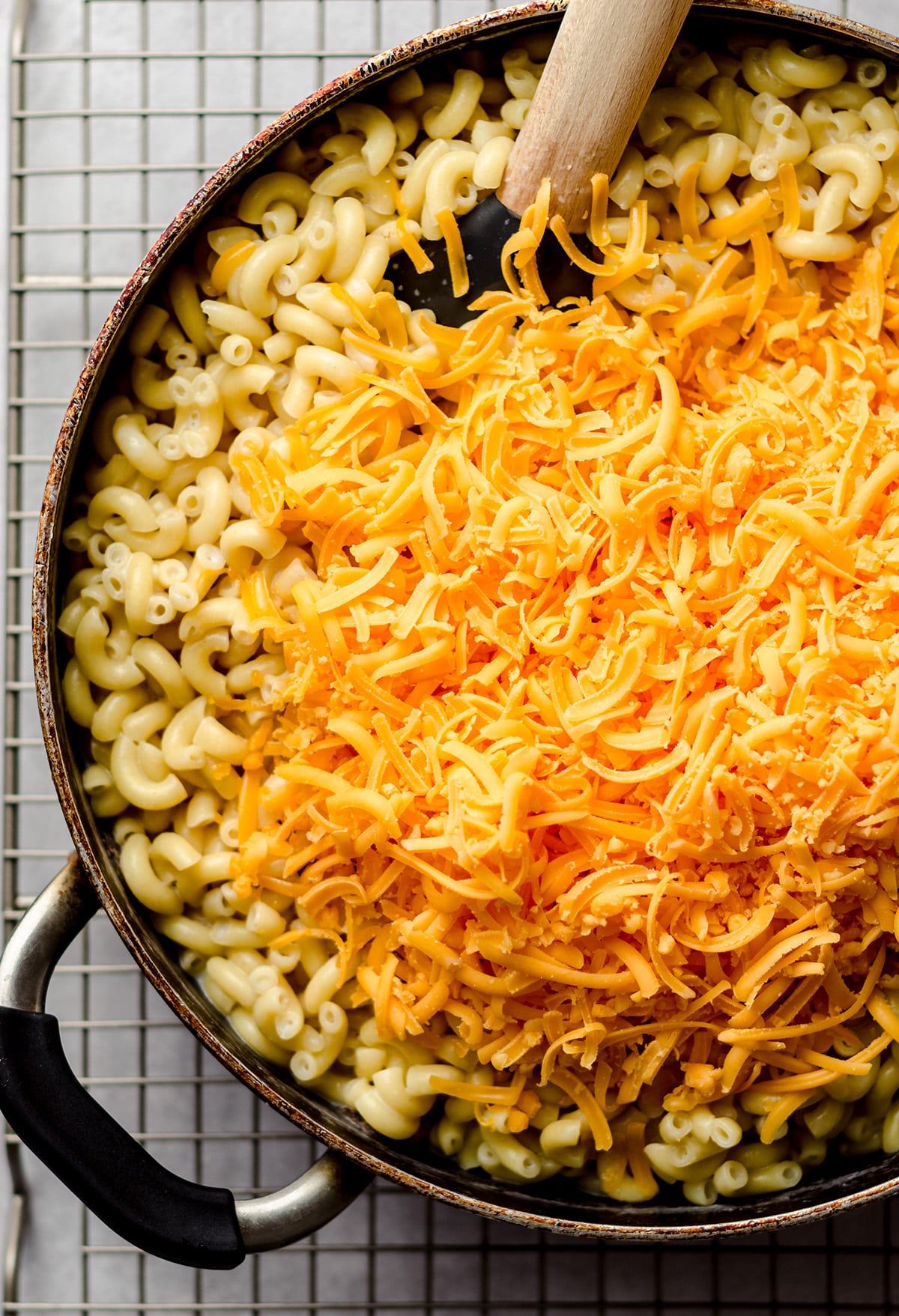 An overhead view of a skillet with cooked macaroni, topped with shredded cheese.