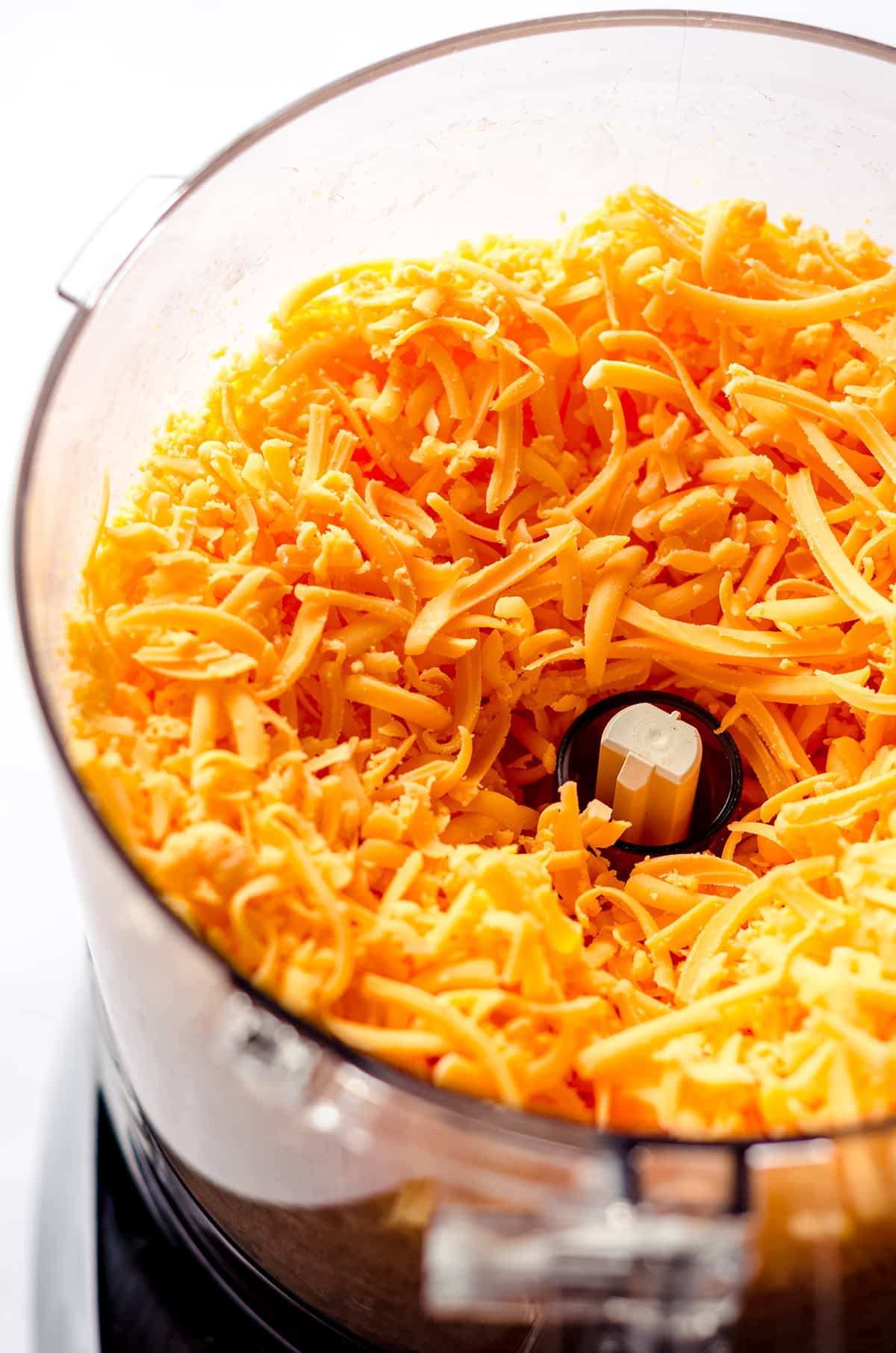 A food processor filled with finely shredded cheese.