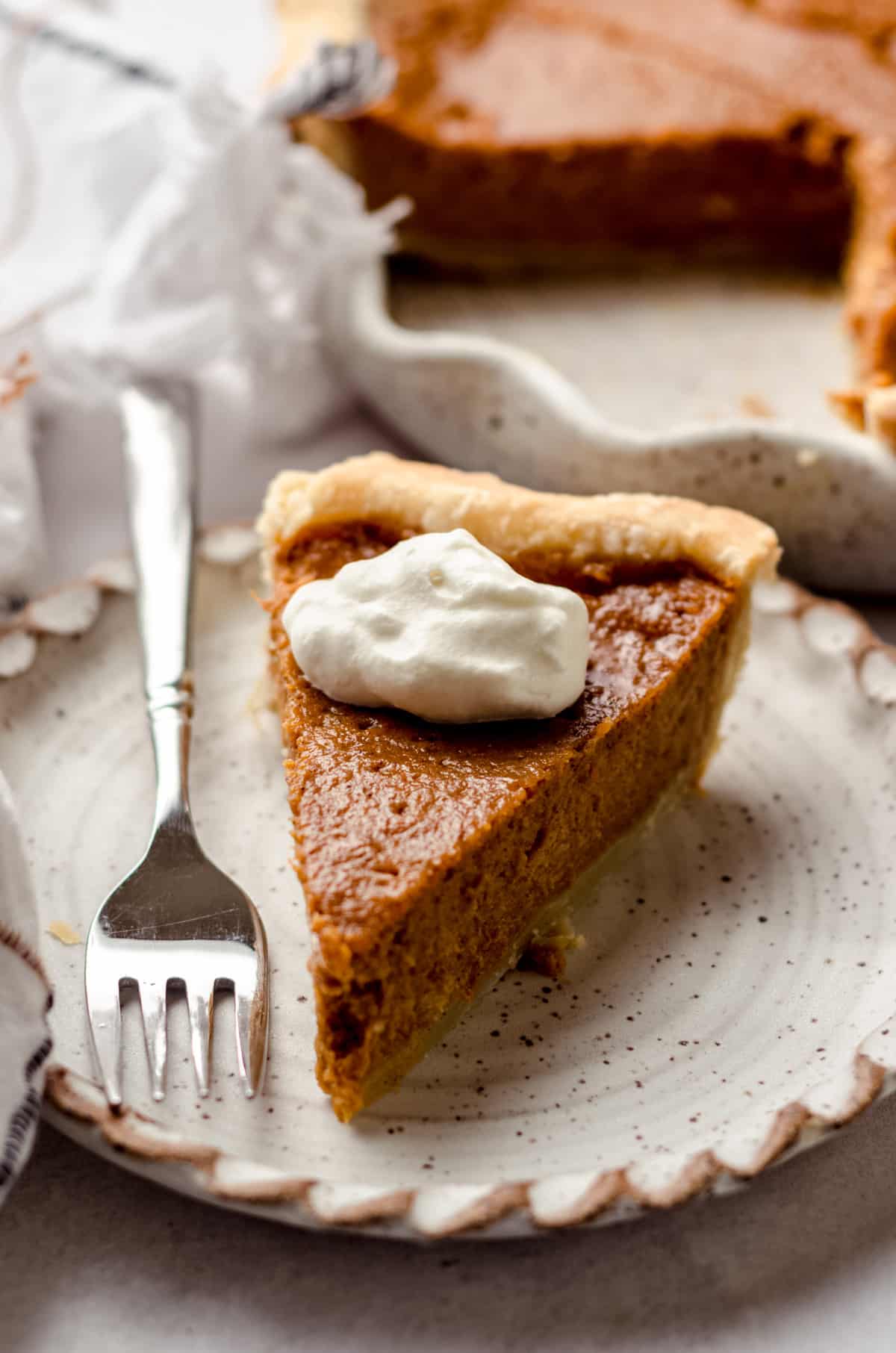 A slice of sweet potato pie on a plate, topped with whipped cream.