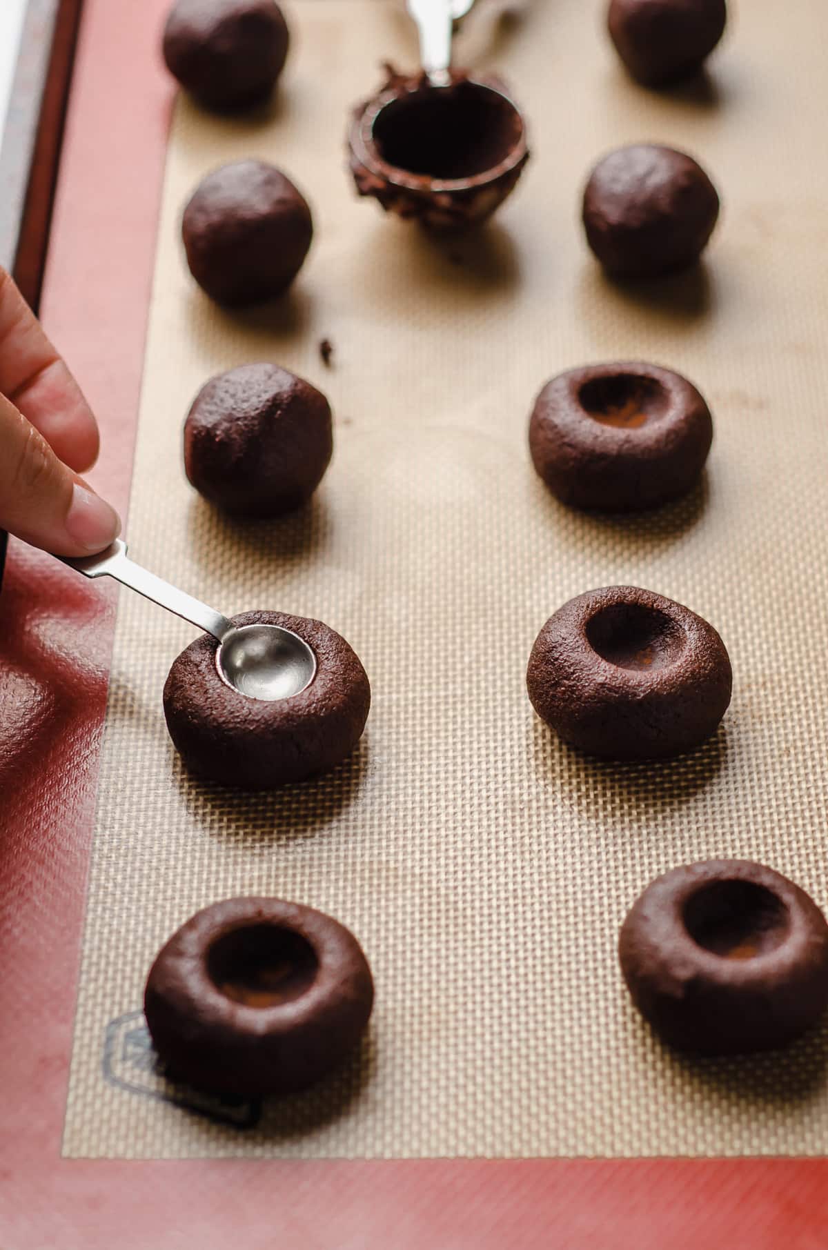 pressing a measuring spoon into chocolate cookie dough balls to make thumbprints