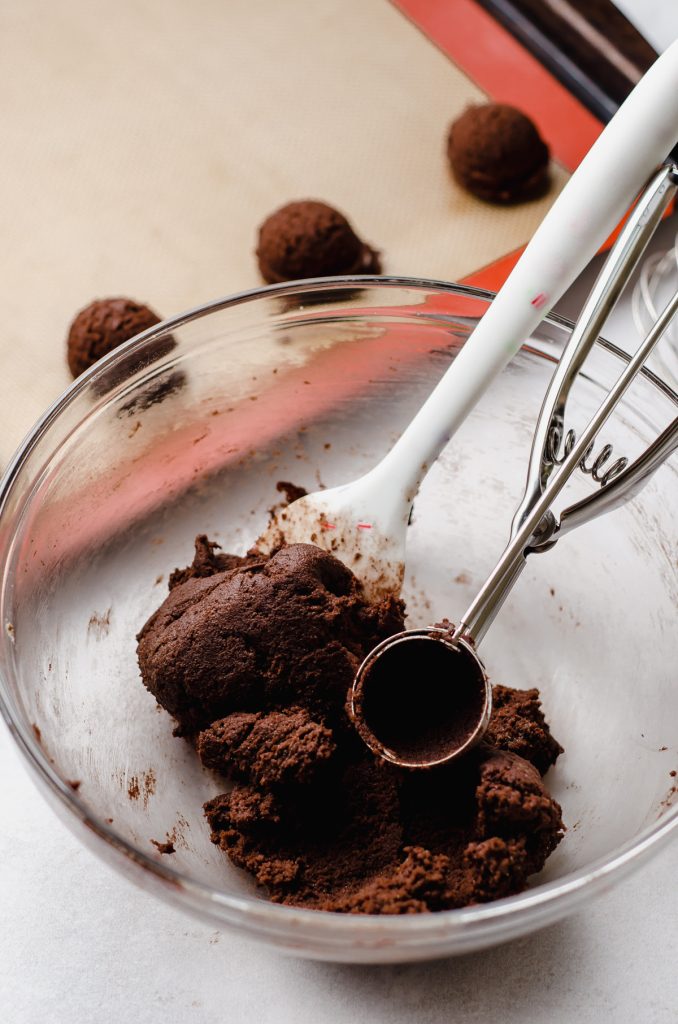 chocolate cookie dough in a bowl with a spatula and a cookie scoop