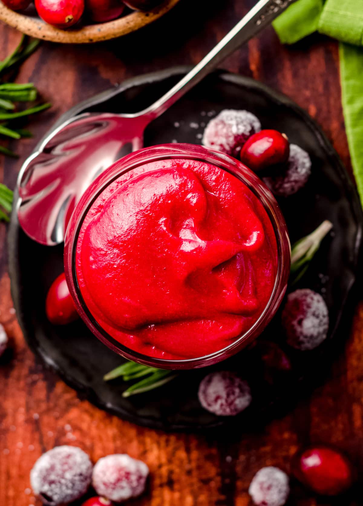 aerial photo of a jar of cranberry curd on a plate with rosemary and sugared cranberry garnish