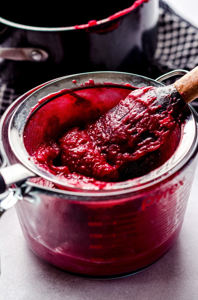 spatula pressing cranberry curd through a mesh strainer