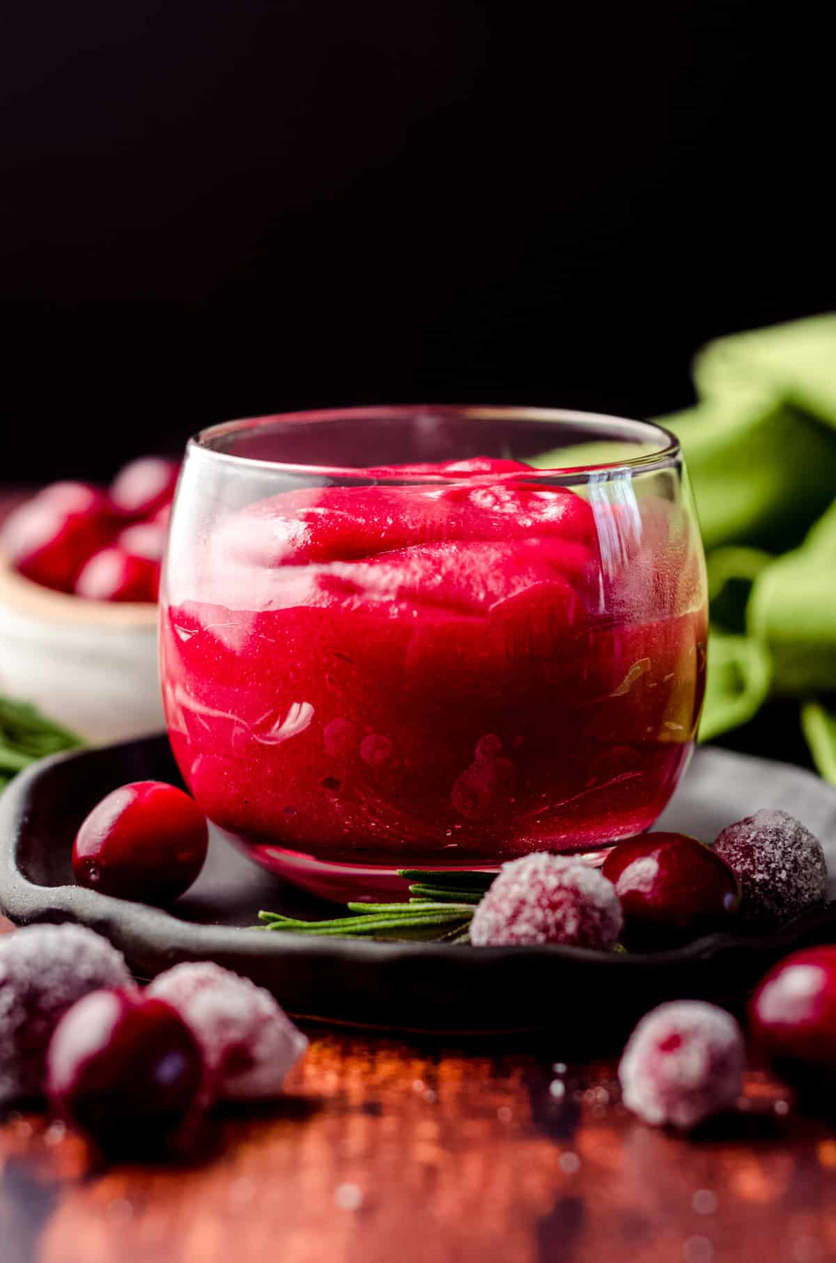 a jar of cranberry curd on a plate with rosemary and sugared cranberry garnish