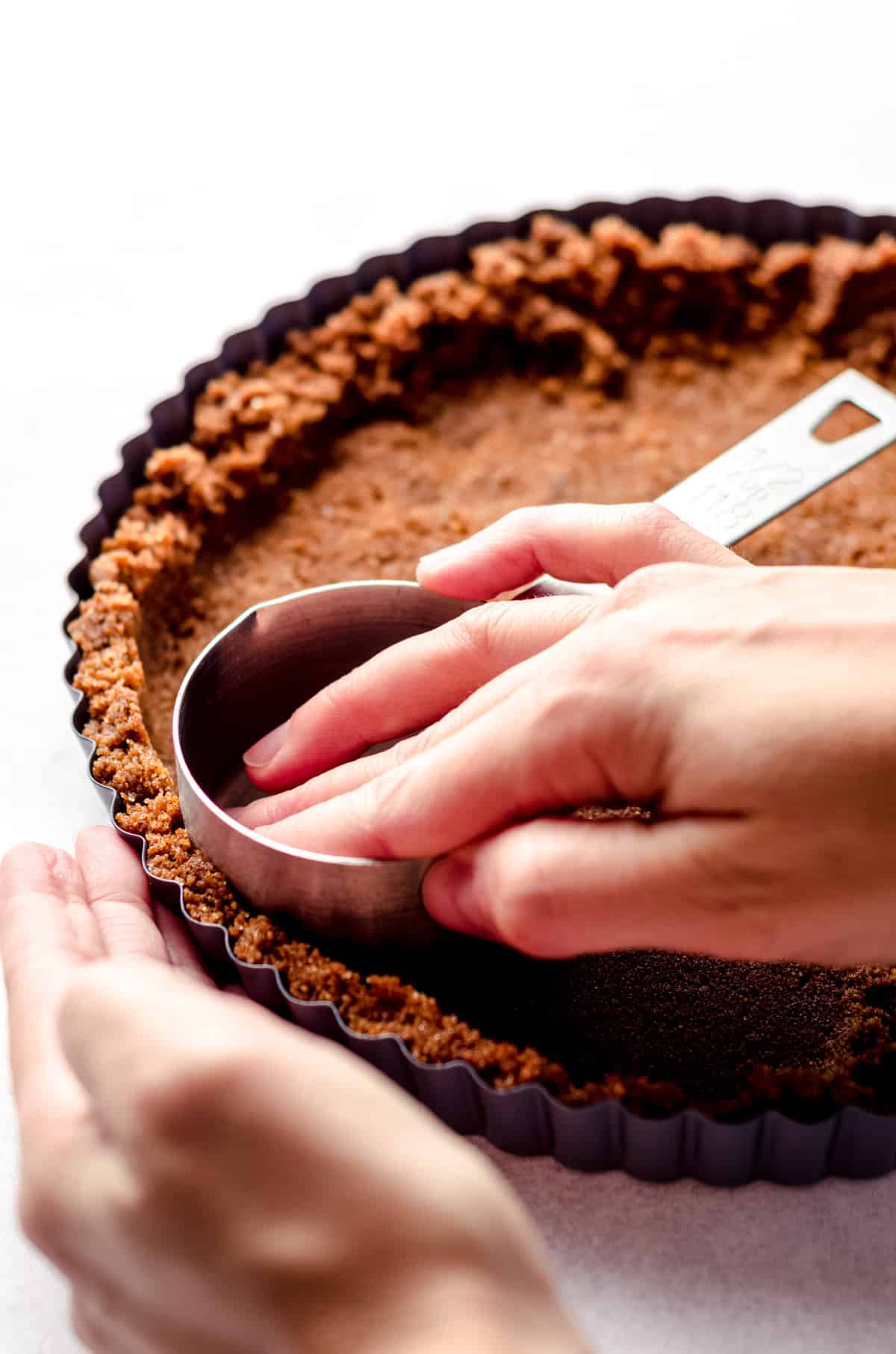 Using a measuring cup to pack down a gingersnap crust.