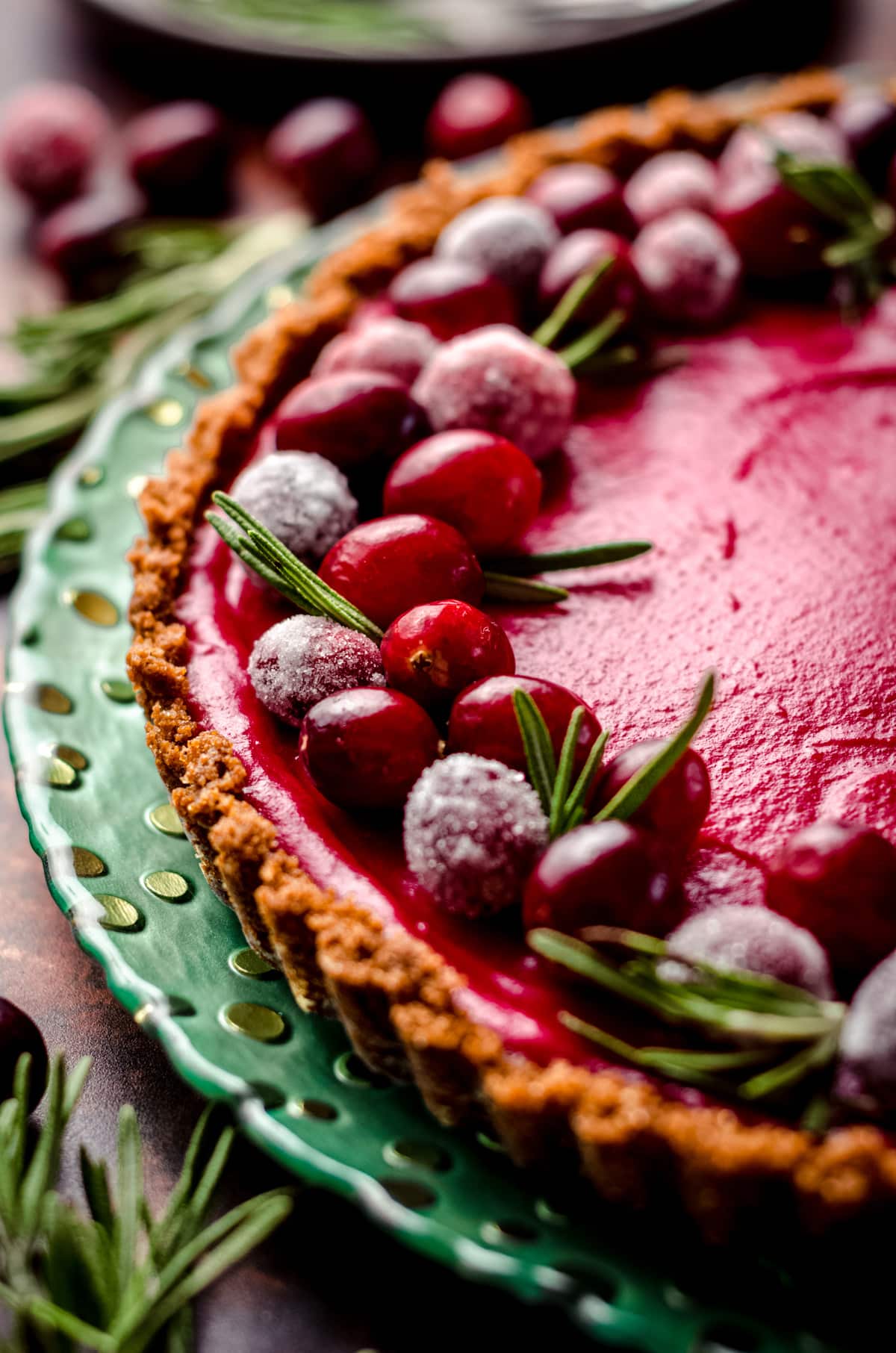 A close up of a cranberry tart garnished with rosemary and sugared cranberries.