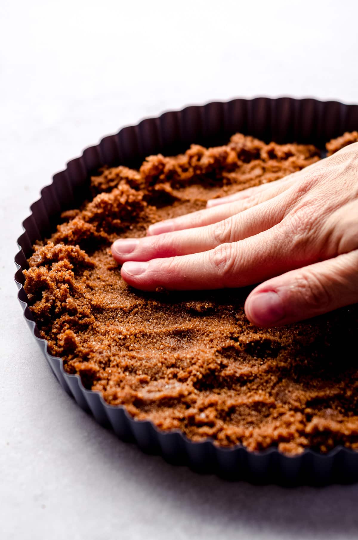 Pressing a gingersnap mixture into a tart pan.