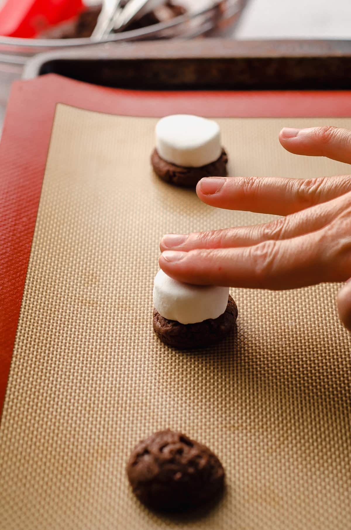 hand pressing a marshmallow onto the top of a hot cocoa cookie