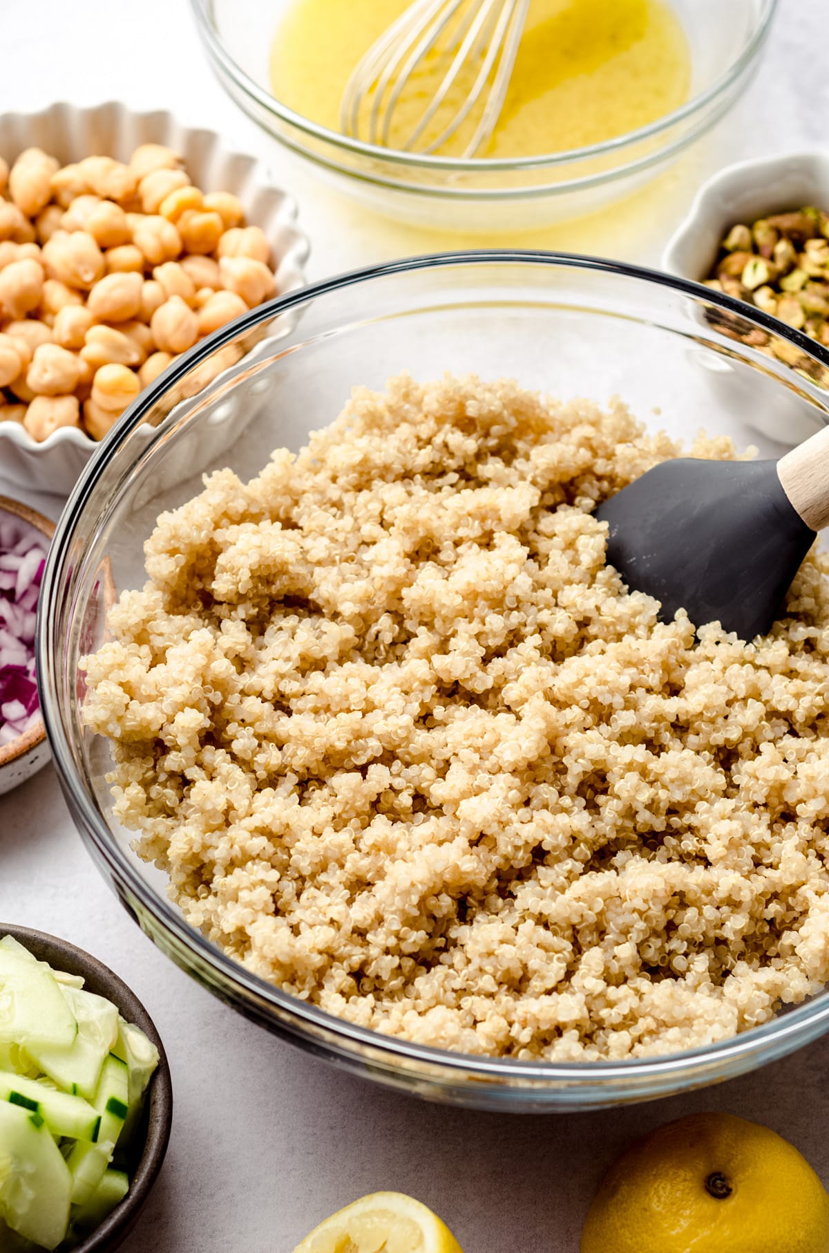 a bowl of cooked quinoa sitting in a glass bowl. Some other ingredients are surrounding it in their own bowls.