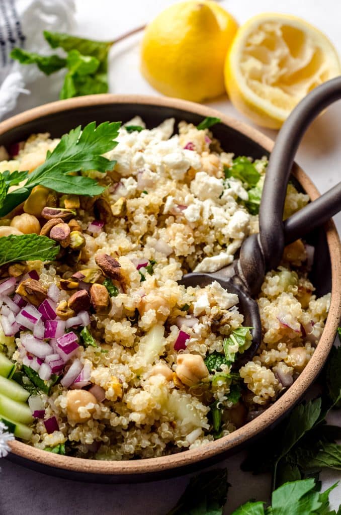 Close up of a wooden bowl filled with the Rachel salad. Ypu can see all the red oinions and cruncy pistachios. There is also quinoa, cucumber, feta  and mint.