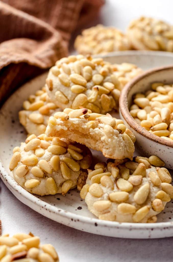 A plate of pignoli cookies with a bite taken out of one.