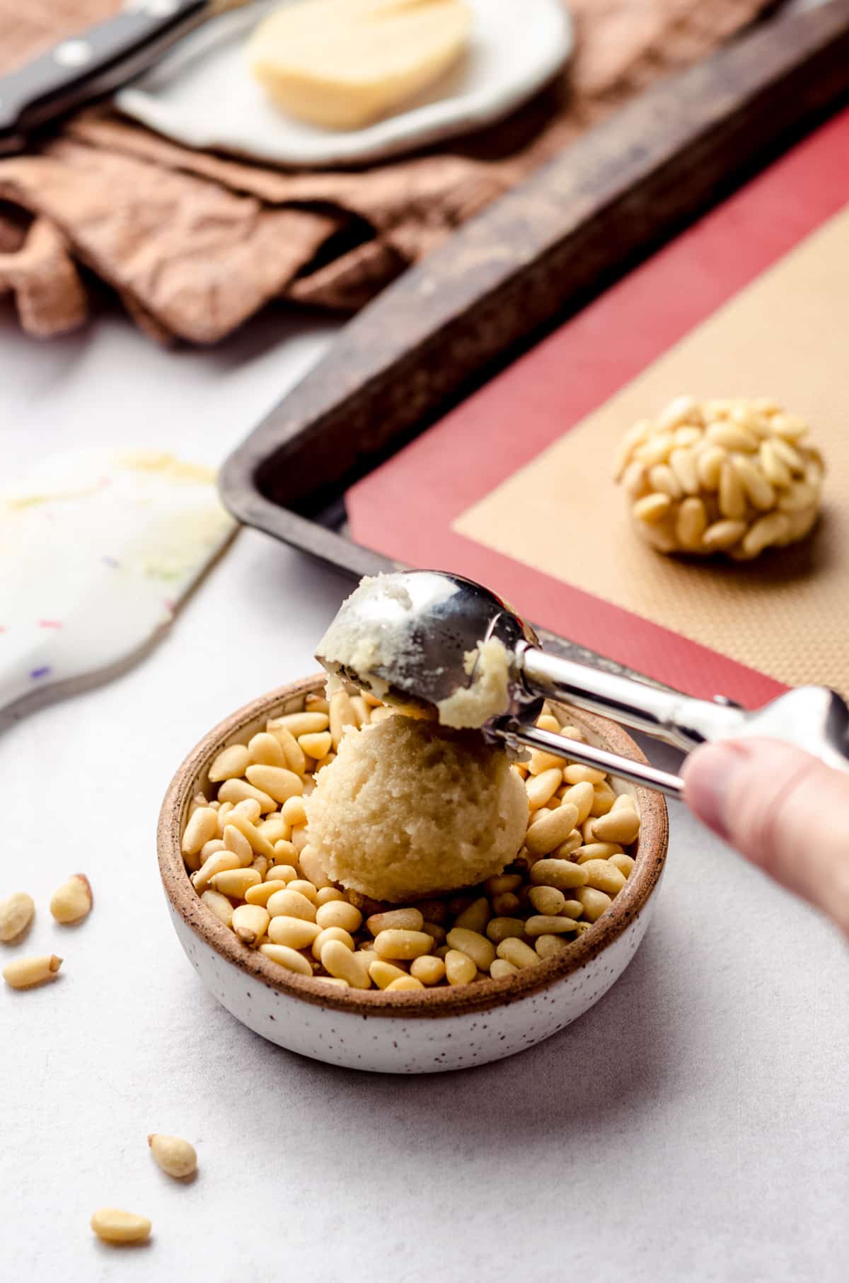 Adding a scoop of cookie dough to a bowl of pine nuts.