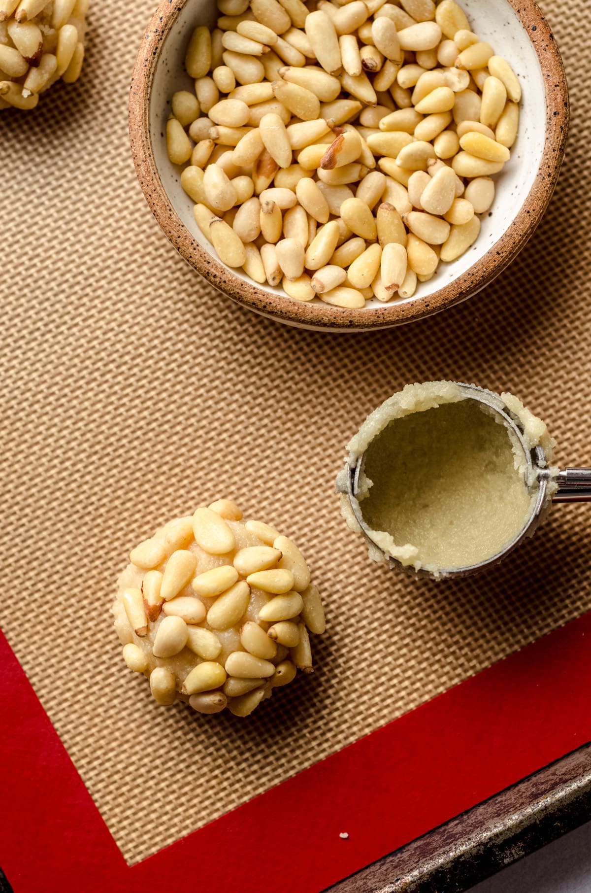 Placing a pine nut coated pignoli cookie on a parchment lined baking sheet.