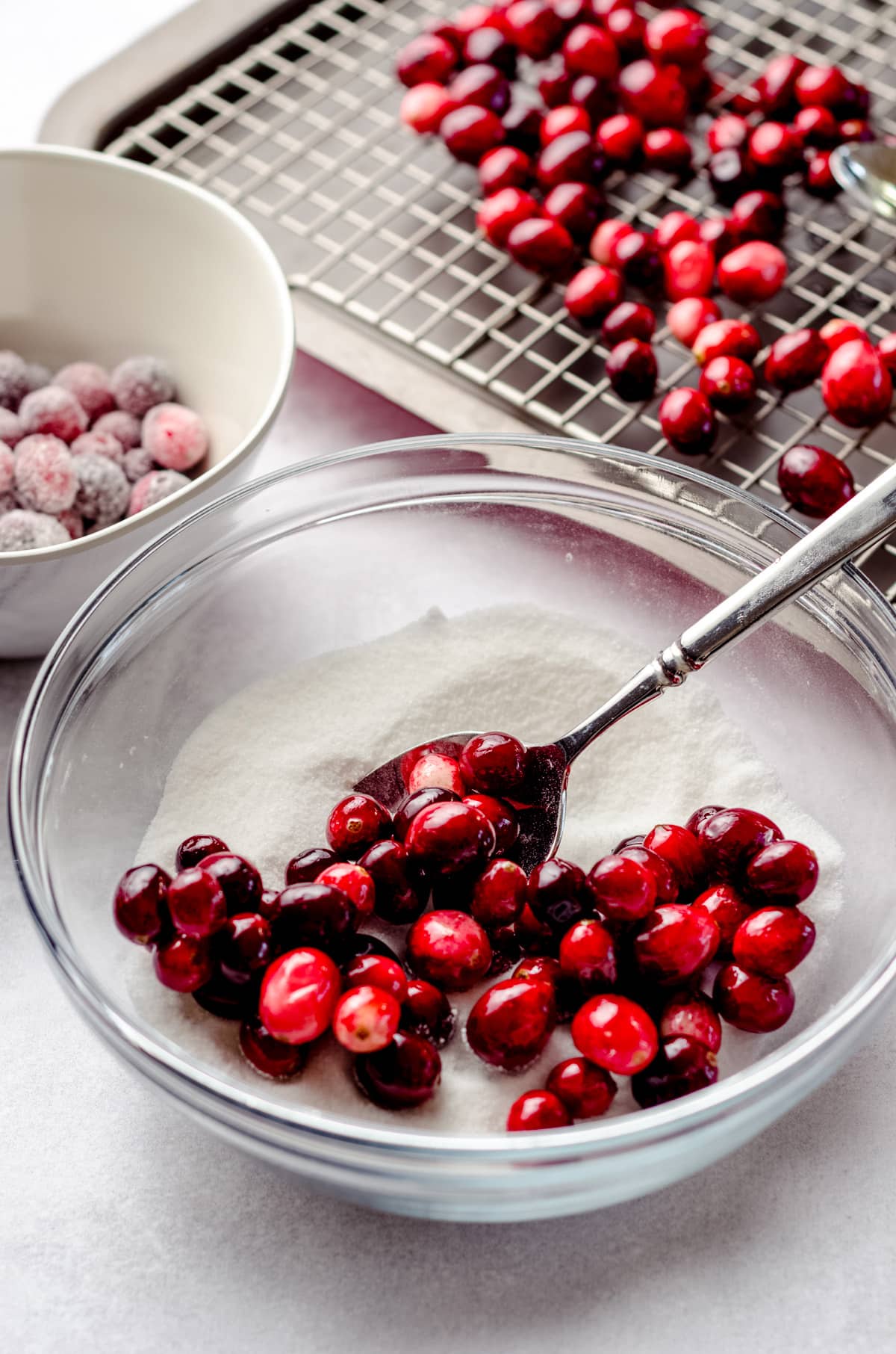 sugared cranberries in a bowl with a spoon to coat in sugar