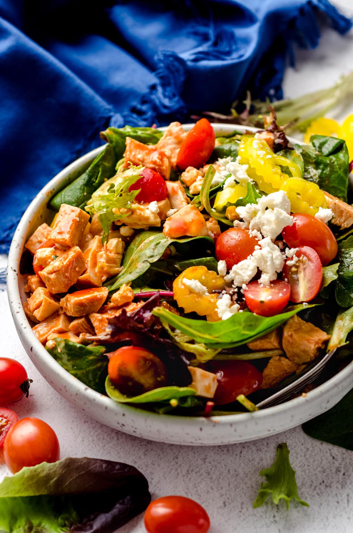 A buffalo blue salad in a bowl with tomatoes and lettuce scattered around the bowl.