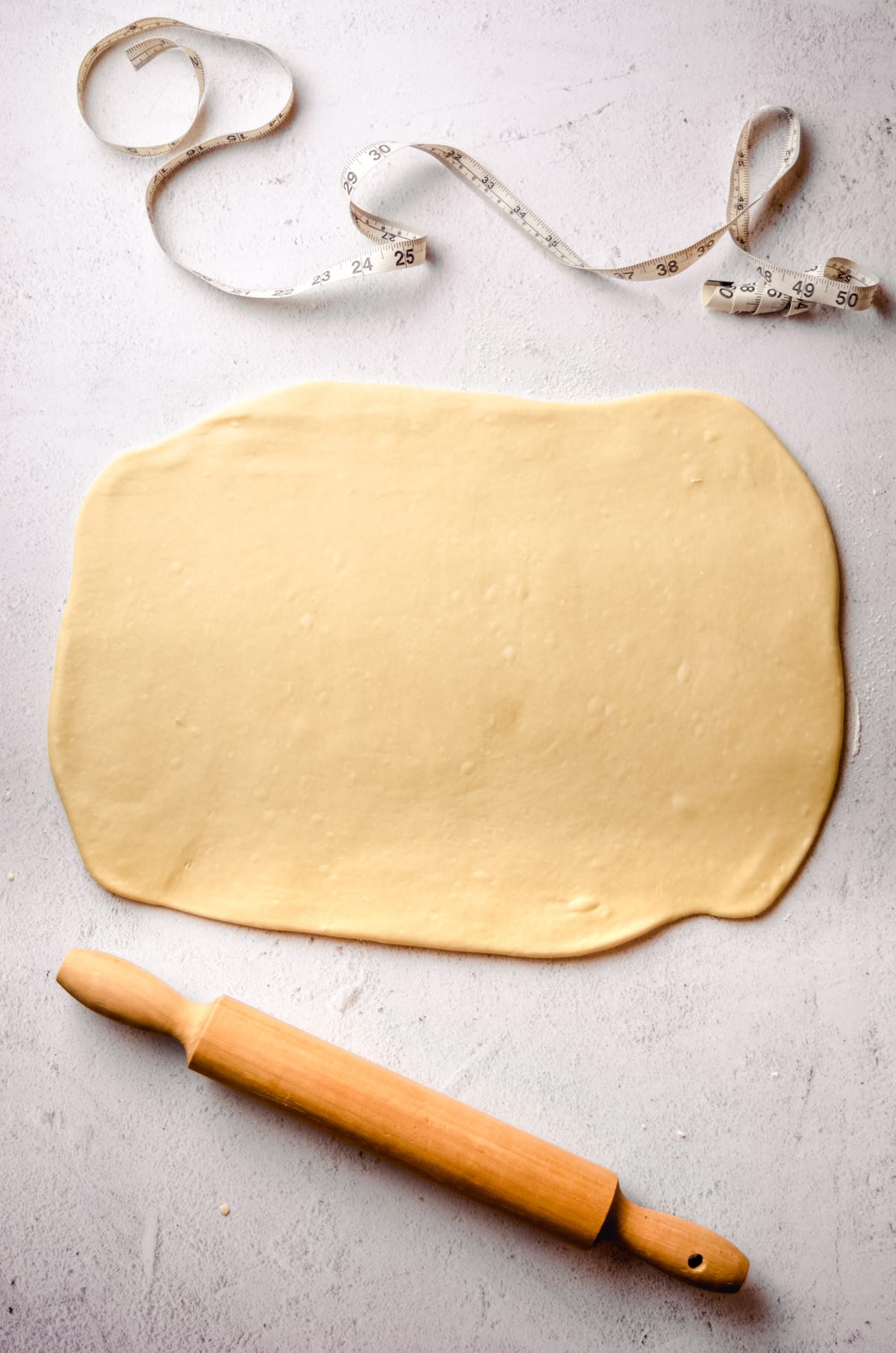 Cinnamon roll dough rolled out into a rectangle with a measuring tape and rolling pin.