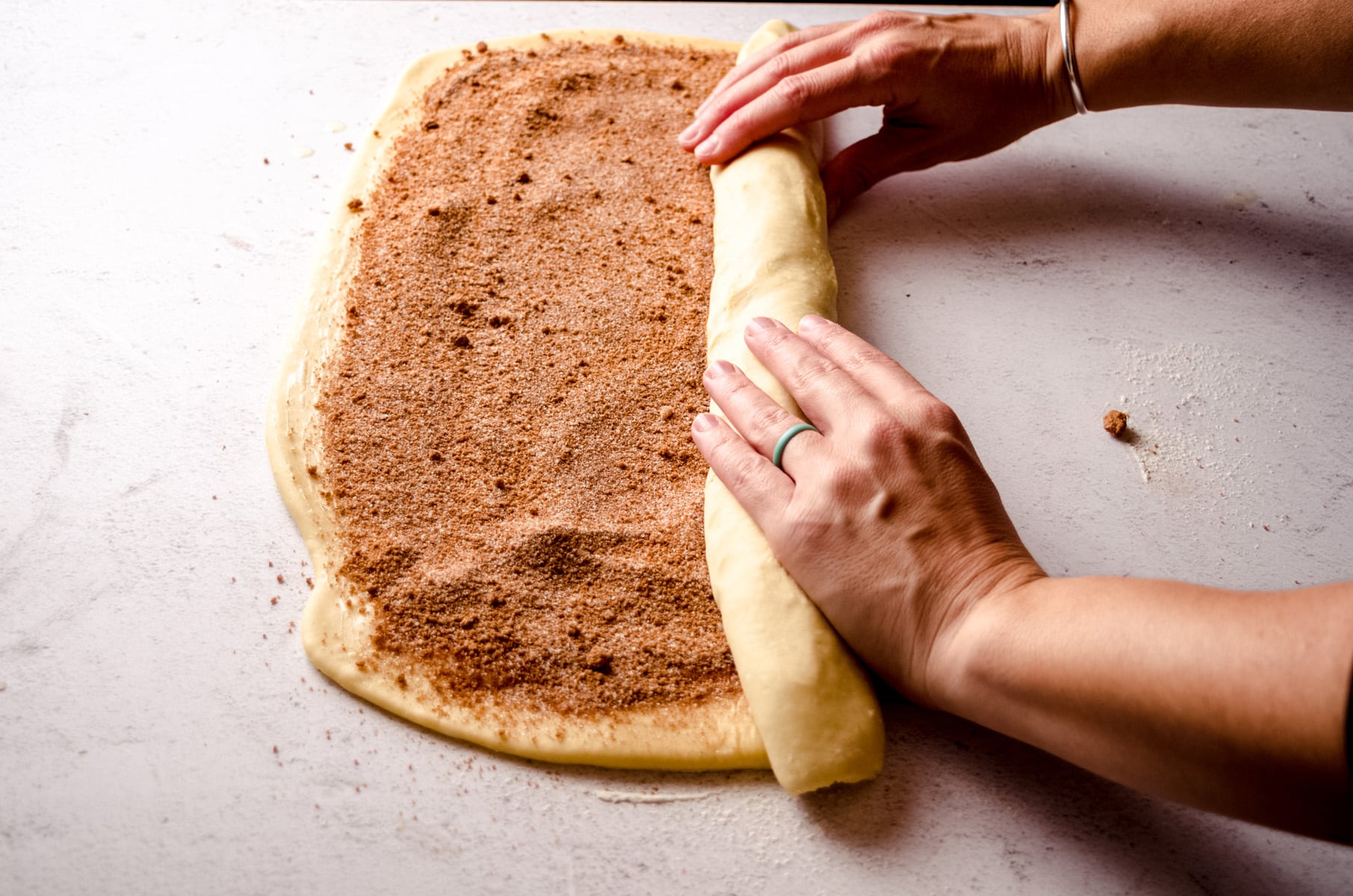Hands rolling up a log of cinnamon roll dough.