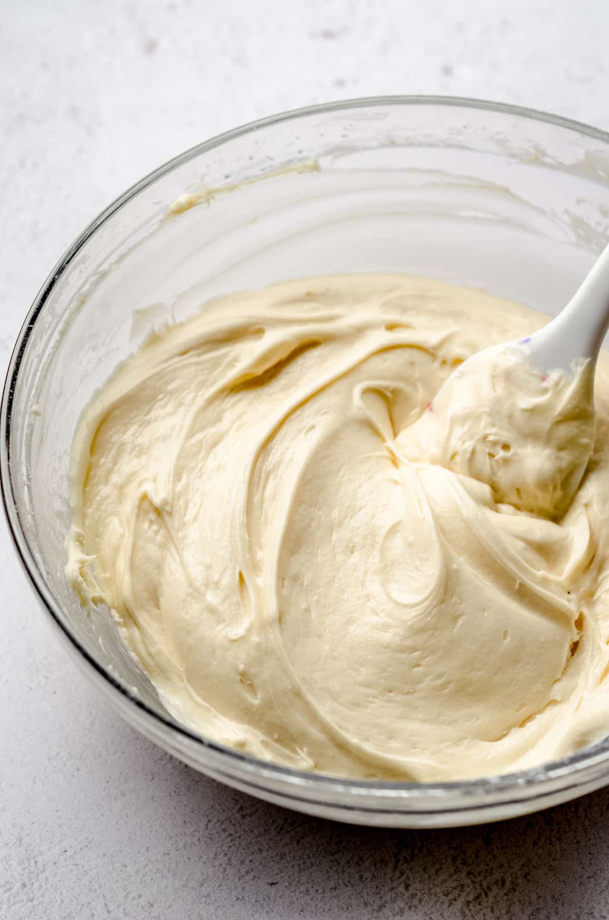 A glass bowl of cream cheese frosting with a spatula in it.