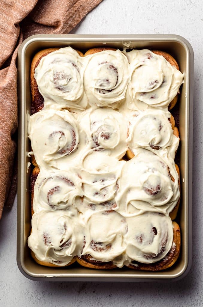 Aerial photo of homemade cinnamon rolls with cream cheese frosting in a baking dish.