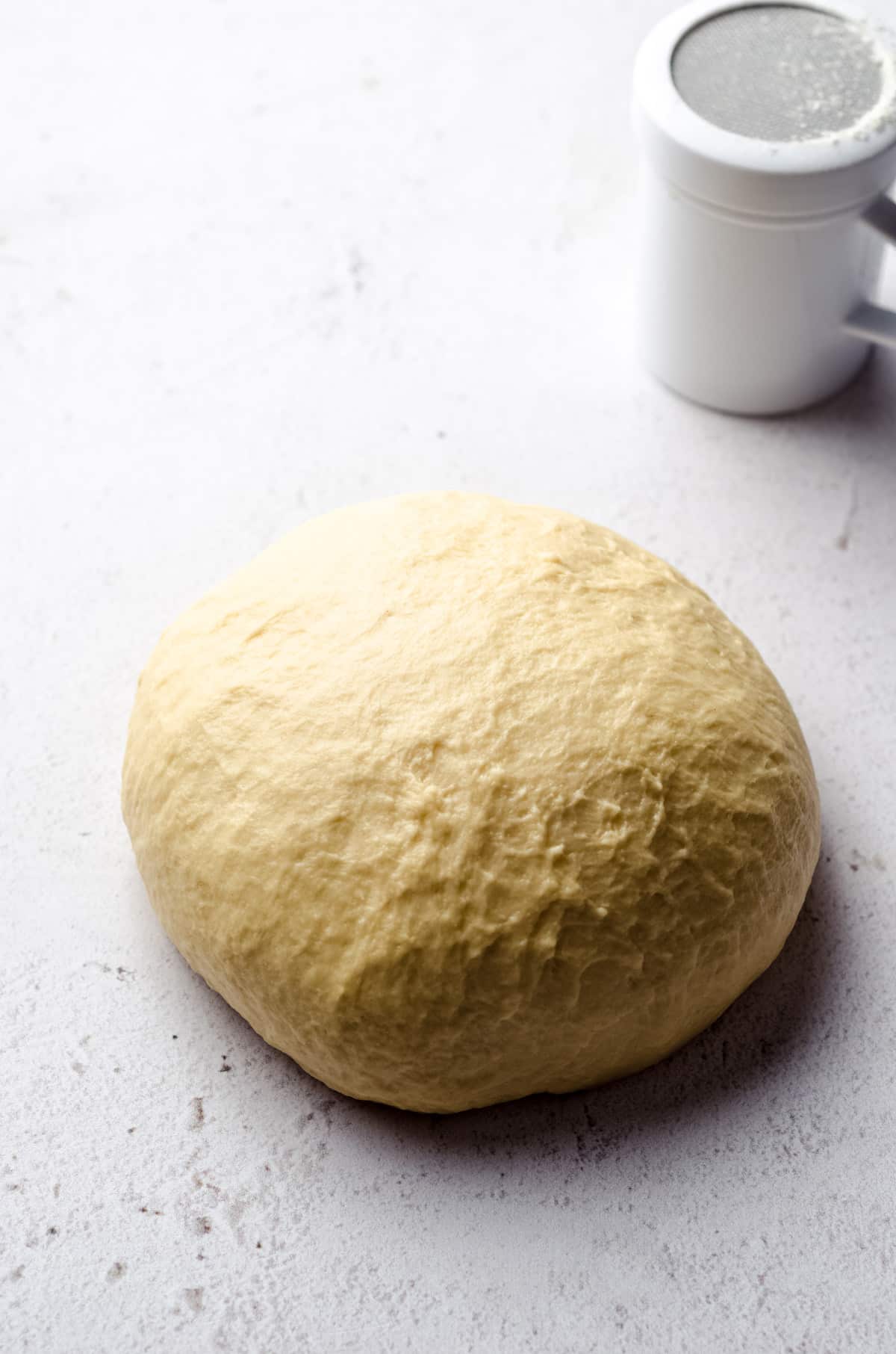 Kneaded enriched yeast dough on a white surface with a flour dredge in the background.