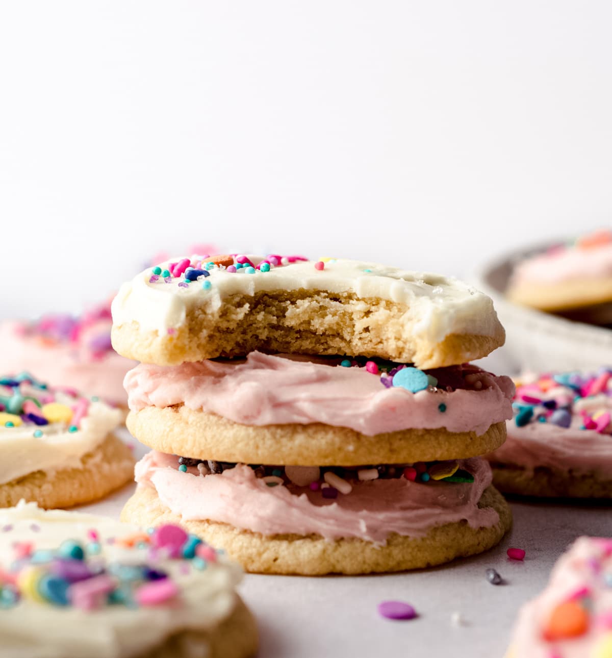 stack of frosted sugar cookies with a bite taken out of the one on top