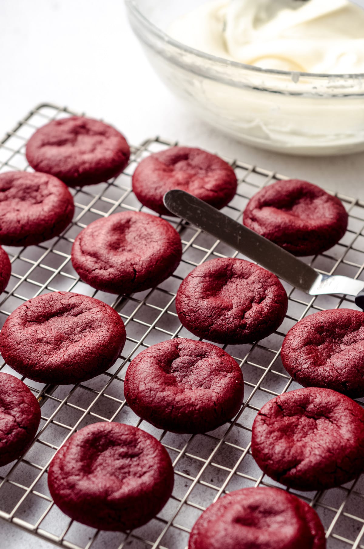 Lots of red velvet cookies, after being baked, are left to cool on a silver wire rack.