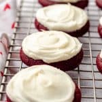 red velvet cookies, topped with cream cheese frosting on a wire cooling rack
