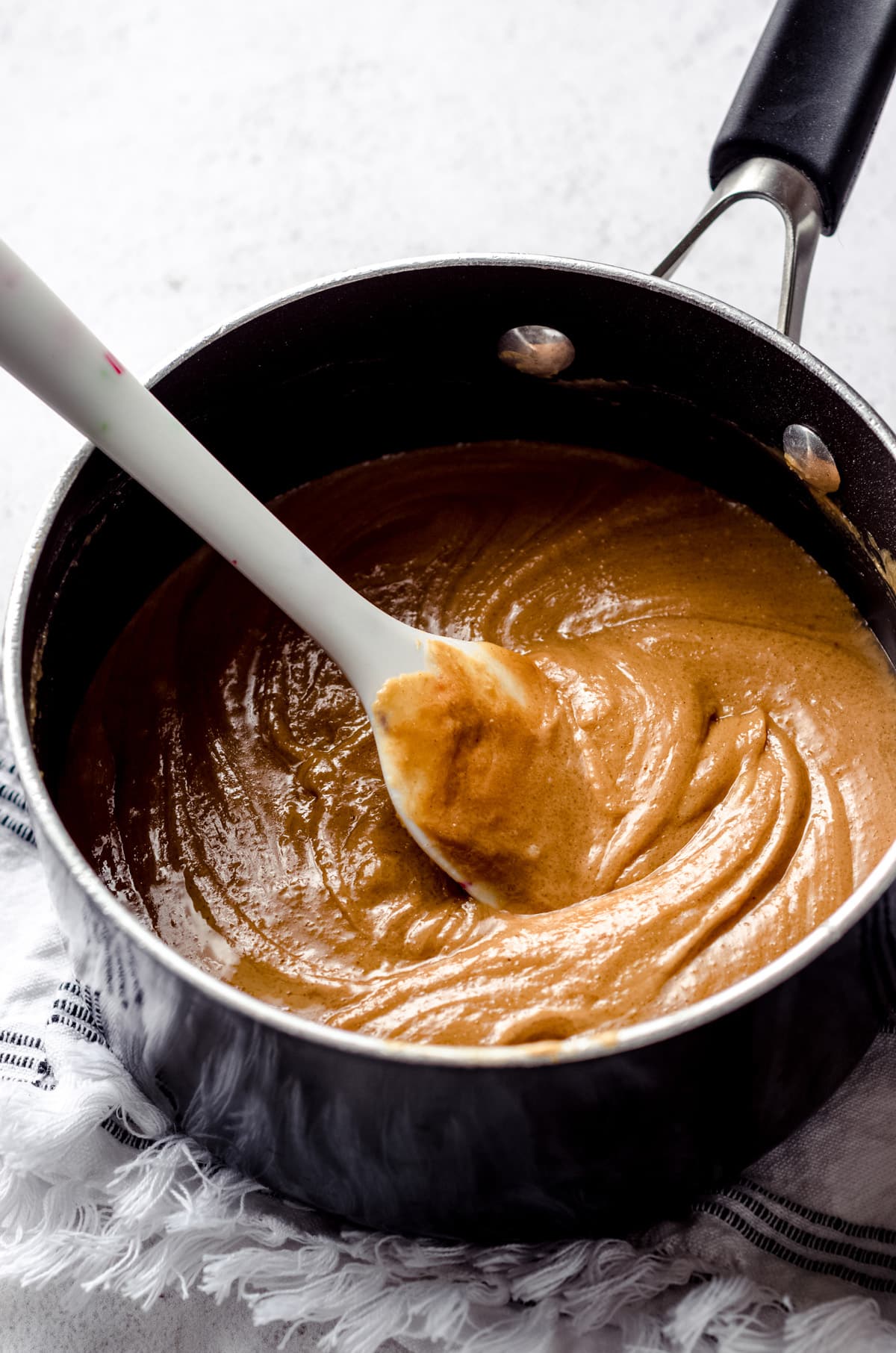 Melted peanut butter mixture for scotcharoos in a saucepan with a spatula.