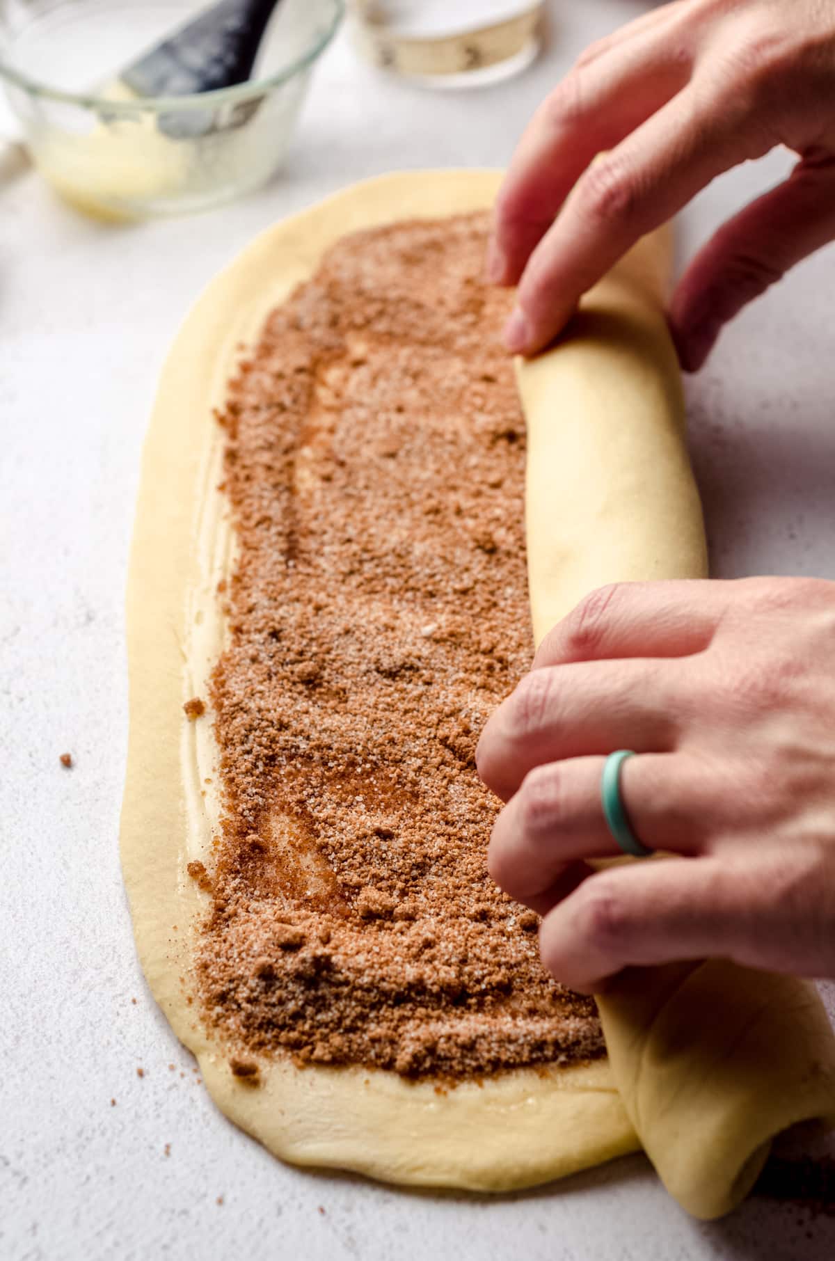 Hands rolling up a log of cinnamon roll dough.