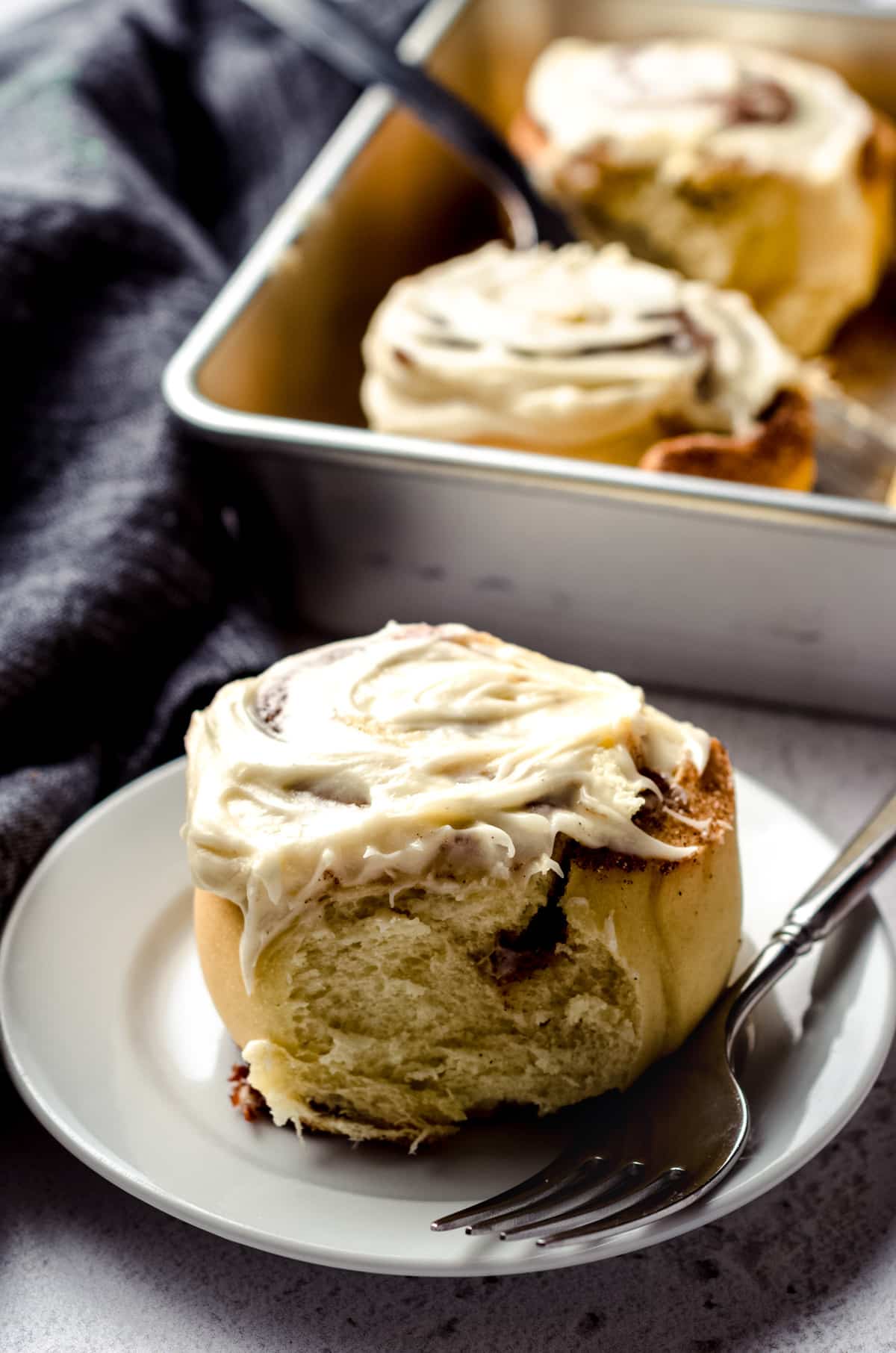 A fluffy cinnamon roll with cream cheese frosting on a plate with a fork.
