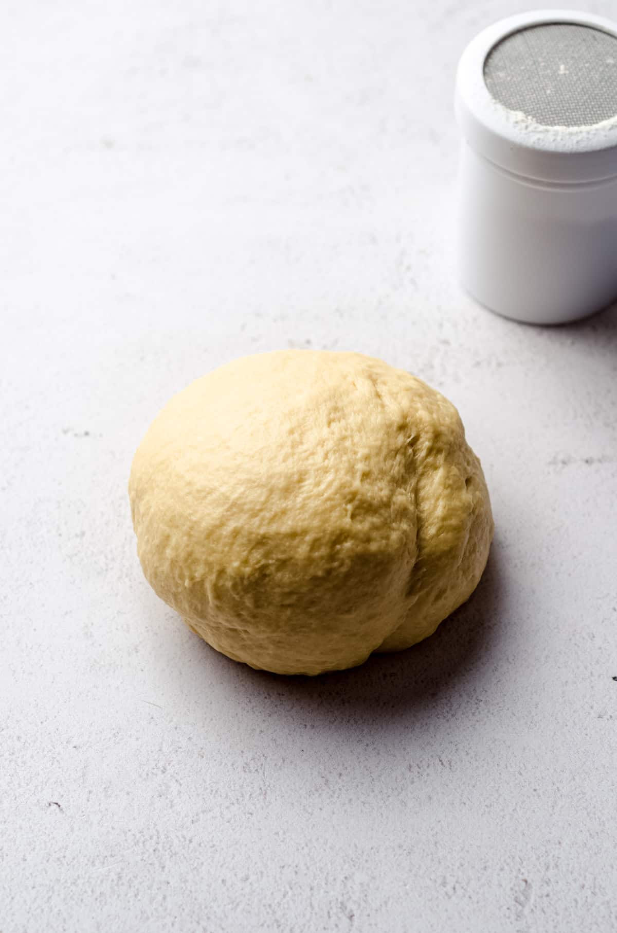 Kneaded cinnamon roll dough on a surface with a flour dredge in the background.