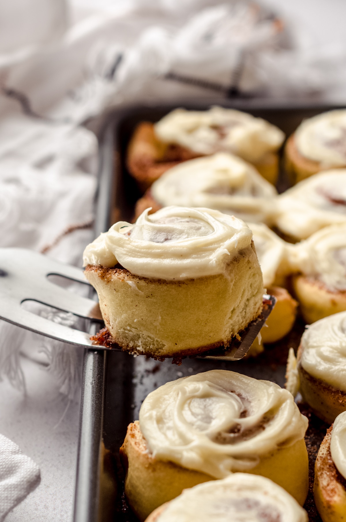 A spatula lifting a mini cinnamon roll out of a baking dish.