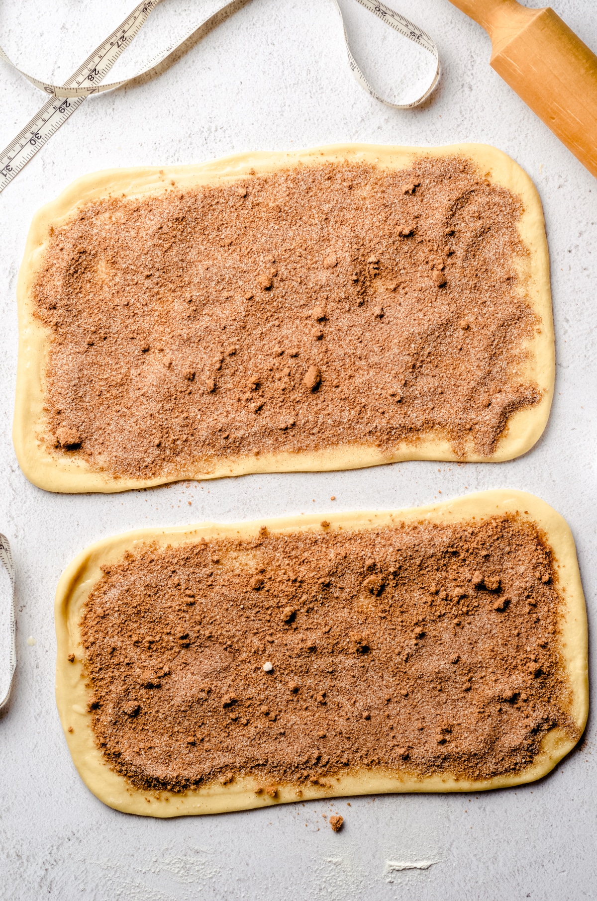 Two rectangles of cinnamon roll dough with filling spread onto them.