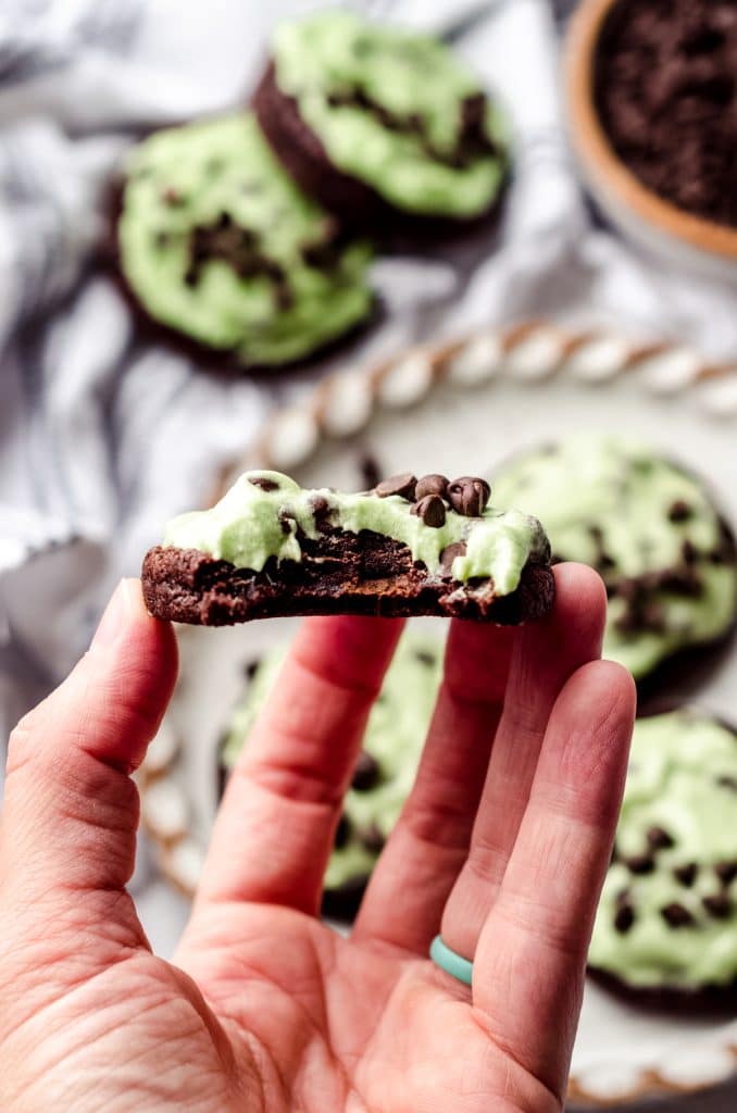A hand holding a mint chocolate chip cookie that is missing a bite. 
