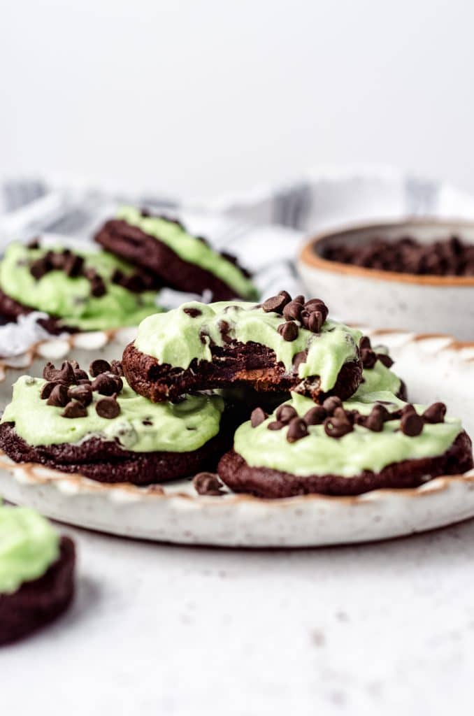 Mint chocolate chip cookies stacked on a plate with one cookie missing a bite.